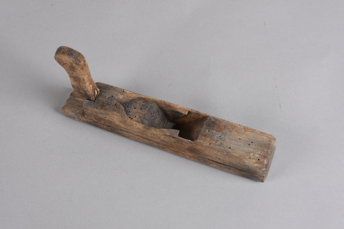 Høvel med rektangulær stokk, horn (handtak) med avrunda ende. Stokken er svakt runda på tvers på undersida. Har spor for høveljern og kile. Skoren dekor på toppen framom sponutkastet.