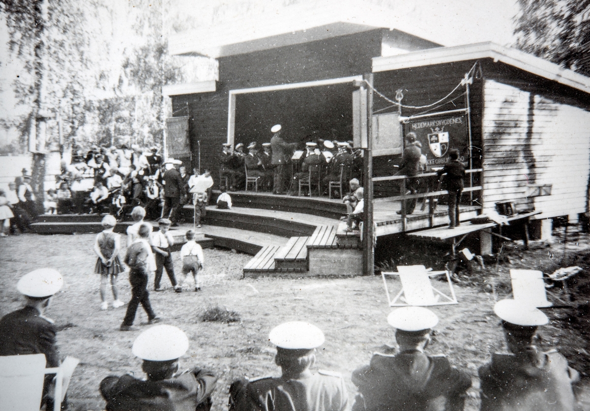 Musikkstevne på Tangenodden. Danseplass, musikkscene. Fane for Hedmarkbygdenes Musikkforbund.