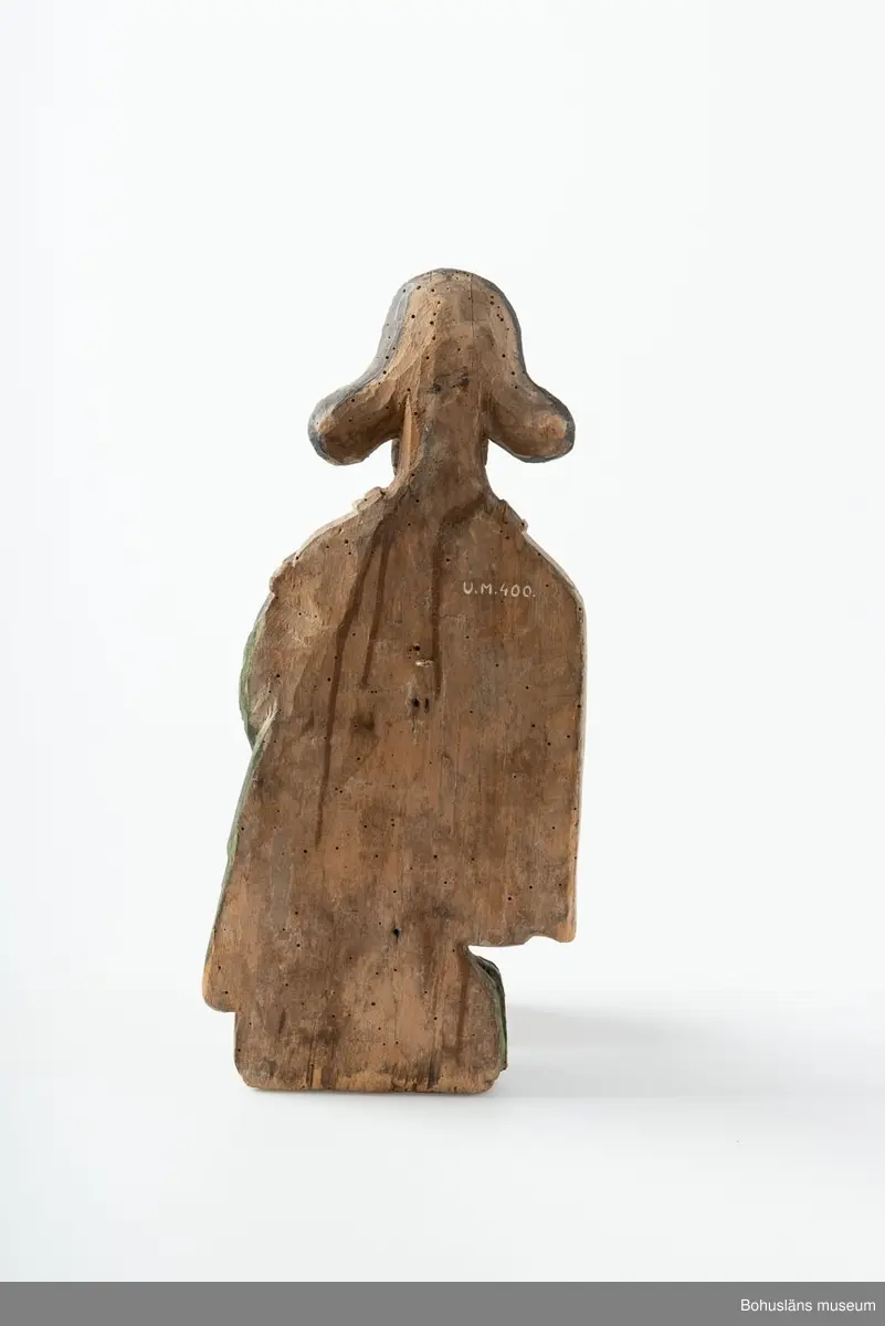 Evangelisten Matteus, nischbild från predikstol. Vid fötterna en ängel. Skägg och hår kraftigt accentuerade. 
Från okänd kyrka i Bohuslän. 
Nischbild från predikstol tillsammans med skulptur UM000399.

G:14 i 1869 års tryckta katalog:
Träbeläte af S:t Matheus.

Knut Adrian Andersosns Katalog I De kyrkliga samlingarna I:124:16:
Träbild av Evangelisten Matheus
44 x 20 cm = G:15 i 1869 års rycka katalog. 
Från tiden efter 1550 i Bohuslän.,

Ur handskrivna katalogen 1957-1958:
S:t Matteus
H.44 cm; i händerna en uppslagen bok, vid fötterna en ängel m. en kalk; manteln grön o. vit, maskhål, färgen ngt. flagn.

Ur Nationalencyklopedin, NE.se: Evangelist
evangelist, benämning på den som enligt traditionen författat något av Nya Testamentets evangelier: Matteus, Markus, Lukas resp. Johannes
I kyrklig bildkonst framställs Matteus och Johannes ofta som äldre män, Markus och Lukas som yngre. Sedan slutet av 300-talet brukar fyra (vanligen bevingade) gestalter, evangelistsymboler, höra ihop med de fyra evangelisterna, antingen bredvid dem eller ensamma, ofta omgivande Kristus eller Lammet. Matteus representeras av en människa, Markus av ett lejon, Lukas av en tjur och Johannes av en örn. Besläktad symbolik möter i tetramorfen ("den fyrgestaltade"), ett bevingat väsen med fyra huvuden (av människa, lejon, tjur och örn), ibland också med motsvarande fötter. Symbolerna är hämtade ur Bibeln. I Hes. 1 skildras hur Hesekiel ser fyra varelser (tetramorfer) kring Guds tronvagn. I Johannes vision i Upp. 4:6-7 har de fyra varelserna kring tronen endast ett ansikte vardera: ett lejon-, tjur-, människo- eller örnansikte. Tillämpningen på evangelisterna bygger på en allegorisk tolkning av Upp. 4:6-7, belagd redan hos Irenaeus.