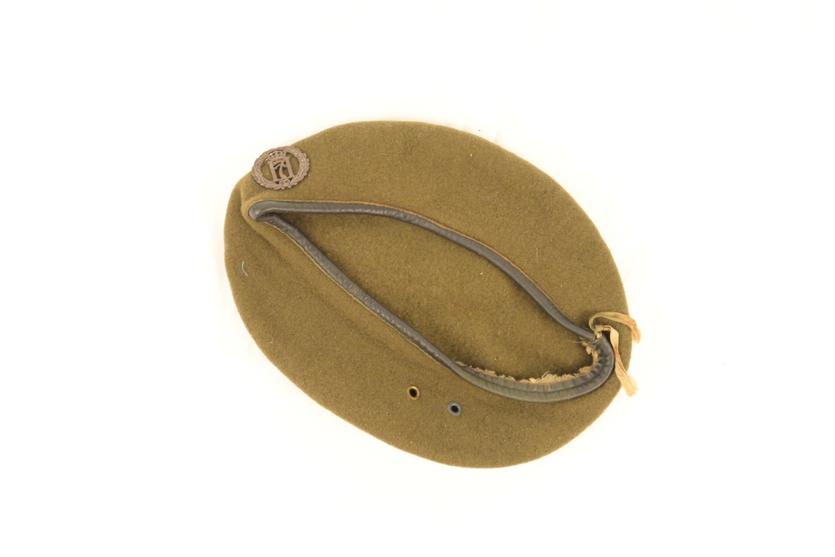 Grønn/brun beret med H7-merke i sølv.