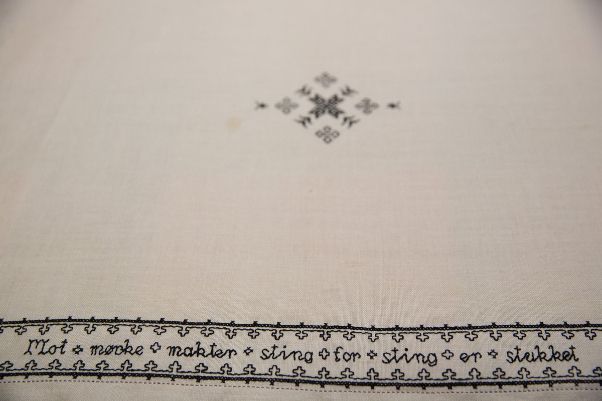 Brodert mønster og bokstaver. Tekst. 

Om symbolikken: Borden med motsatte kors skal symbolisere falne på begge sider under krigen. Her fins referanser til Maginotlinjen og slagene ved Pantelaria, Lampedusa og Midway. Langs kanten rundt er det bodert inn verslinjer.