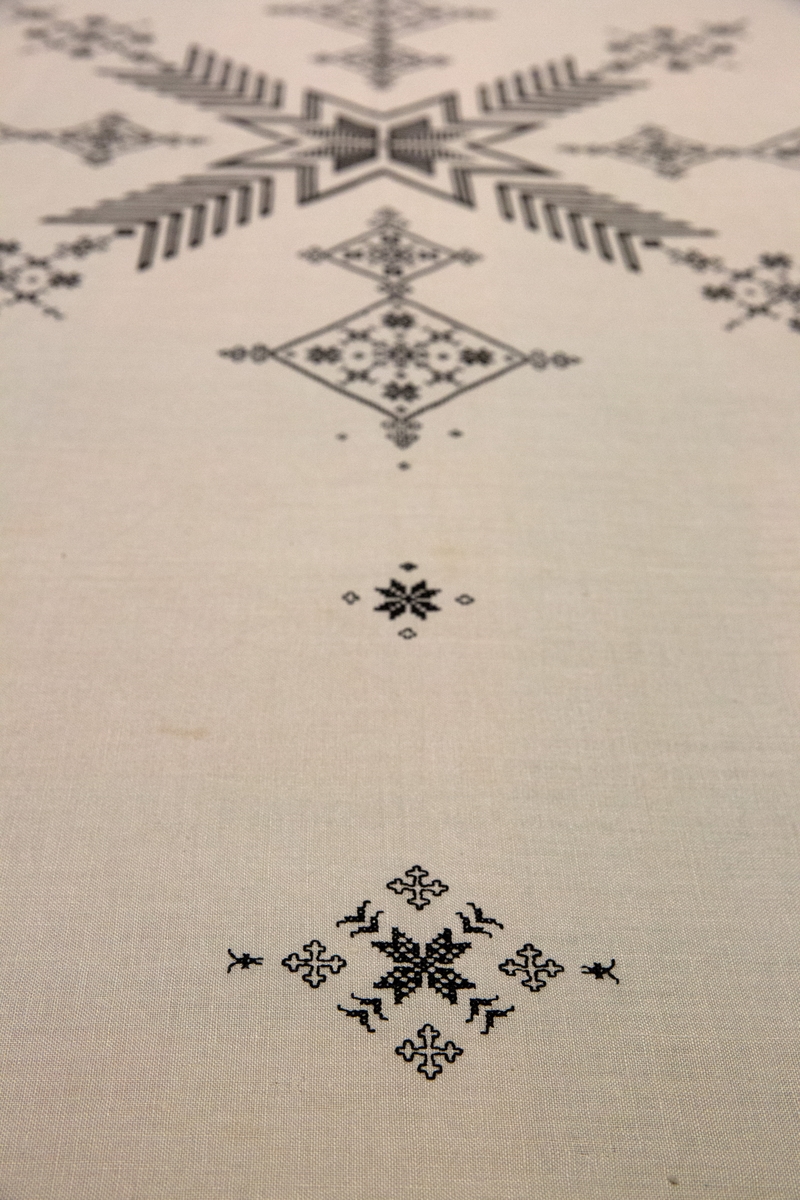 Brodert mønster og bokstaver. Tekst. 

Om symbolikken: Borden med motsatte kors skal symbolisere falne på begge sider under krigen. Her fins referanser til Maginotlinjen og slagene ved Pantelaria, Lampedusa og Midway. Langs kanten rundt er det bodert inn verslinjer.