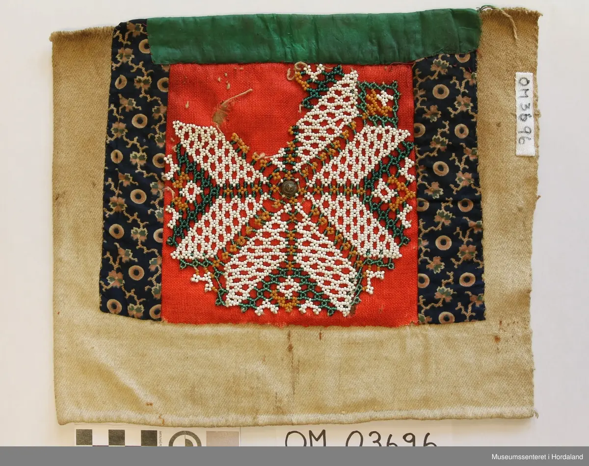 Rektangulær bringeduk med perlenett med åttebladrosemotiv sydd på raudt ullstoff. Perleveven er noko rakna og manglar eit blad. Midt i åttebladrosa er det sydd på ein knapp. Ullstoffet har fleire hol. Grøn silkeband oppe. Blått mønstrete bomullstoff på kvar side sydd på eit kypertvevd naturfarga stoff. Skittent på baksida. Det grøne bandet er sydd oppå eit anna rosafarga silkeband.