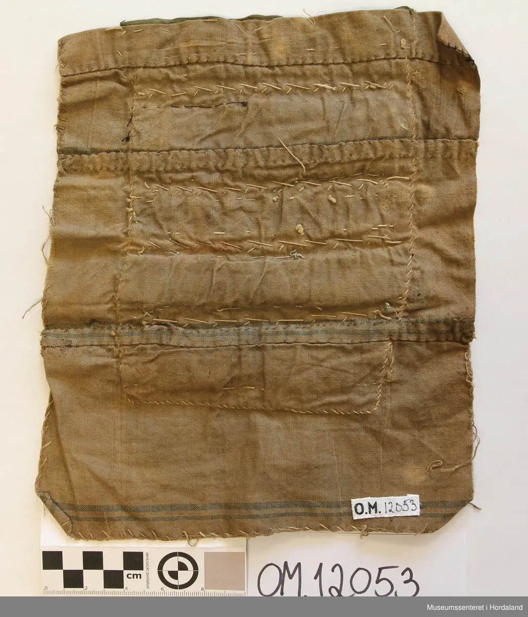 Brungeduk samansett av sylvband og perlebroderi i border. Desse er festa til eit raudt bakstykke av ull. Bakpå der att er det eit større stykke av bomullslerret, sydd saman av 3 remser , har truleg vore kvitt, men er brunt no, med 2 smale blåe striper nedst.
Oppe på framsida har bringeduken fyrst eit grønt silkeband, 2,5 cm breidt. Utanpå der ligg ein sylvknipling. Rett under den er det sydd på nokre småe perlemedaljongar. Så kjem eit breidt (4 cm) forgylt band, ei rad med perlevev, 3 cm, ny rad med forgylt band, 2,5 cm breidt, så dei same perlemedaljongane att, nederst er eit sylvband som det har vore brodert litt på.