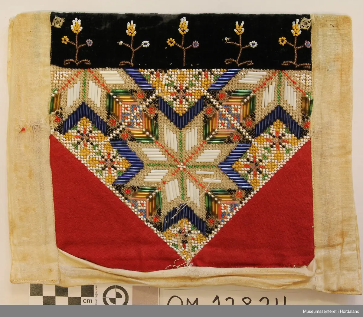 Perlebringekduk med åttebladroser som hovudmotiv. Her er brukt både små perler og ståperler. Perlene er sydde på stramei. Oppe er det ein svart pløyelskant der det er sydd på 5 stiliserte blomstermotiv i perler. Heilt øvst på fløyelstykket på kvar side er det sydd på trykk-knapper for å feste bringeduken til livet. Nedanfor perlene er det sydd på raude tøystykke i bomullsflanell. Utanfor sjølve perlemotivet er det kvitt lerret, også som bakstykke. Inni ligg det ei nokså stiv papp-plate. Bringkluten er velbrukt og slitt og manglar ein del perler.