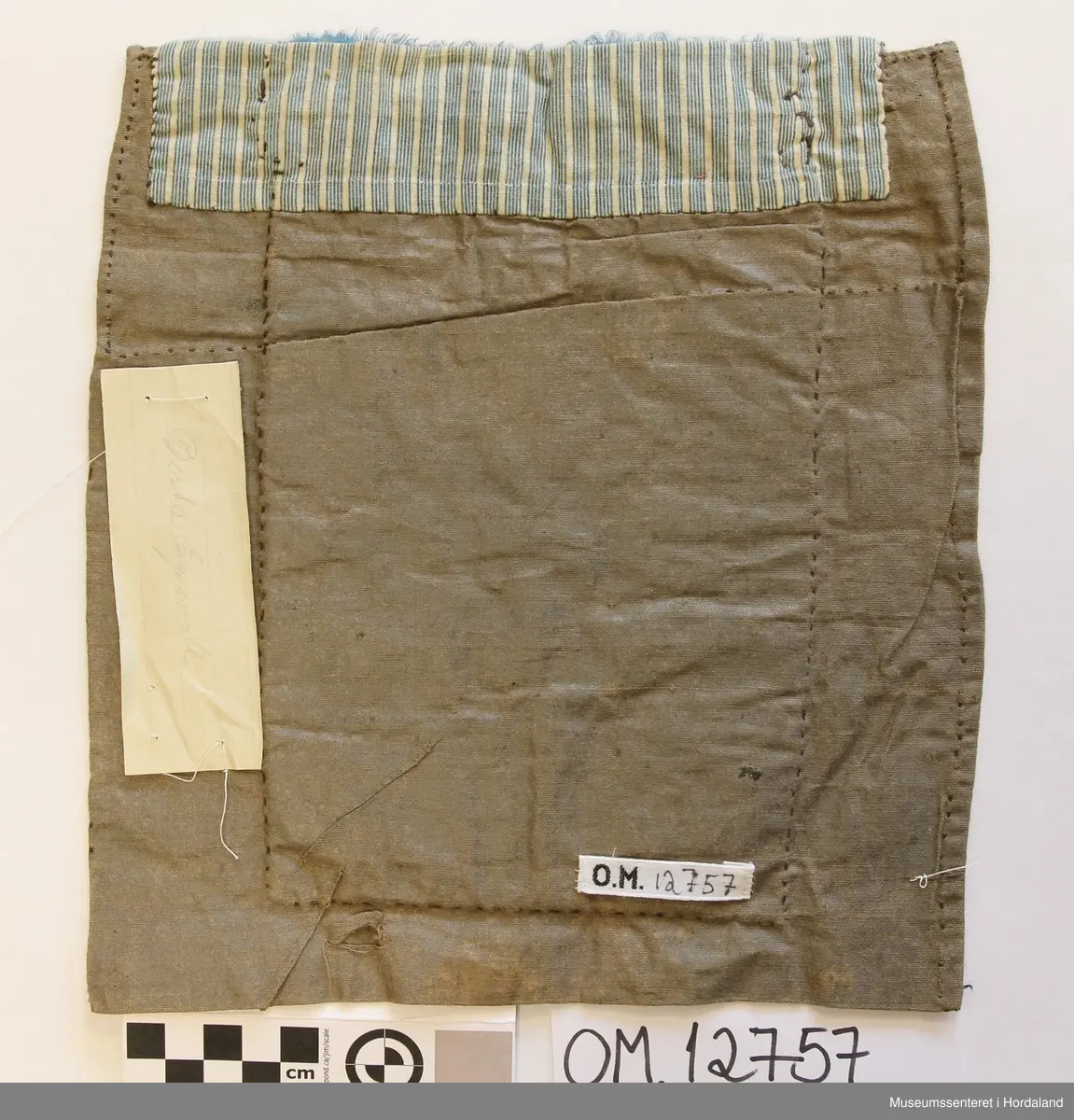 Brodert med ullgarn i plattsaum. Alt er handlaga. Hovudmotiv er små åttebladroser i border. Oppe er det påsydd eit blått silkeband med eit breitt gullband (i forgylt sølvtråd) utanpå silkebandet. Alt er montert på eit tynt, vokset bomullslerret. Oppe på baksida er det eit ekstra bomullstoff (blåstripet). Bokstavane BODM er broderte inn nede på bringeduken i kross-sting.