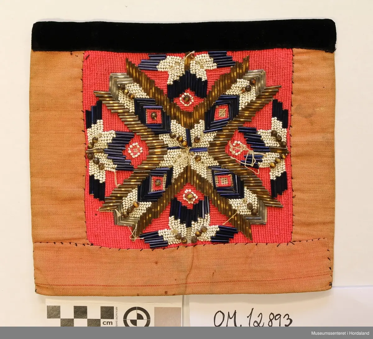 Kvadratisk brystduk i perlebroderi sydd på stramei og broderi innimellom - halve kross-sting. Svart fløyelsband øvst. Brystduk og kanting av eit rosa stoff. Perlebroderiet er sydd av gullfarga og blåe stråperler og kvite småperler og gullfarga store perler i eit åtteblad rosemønster. Mellomromma er fyllt ut av eit broderi (halve kross-sting) i rosa ulltråd.