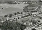 Flygfoto över Vivstavarvs arbetarbostäder, spruthuset och brädgård till höger samt herrgården till vänster. Vykort.