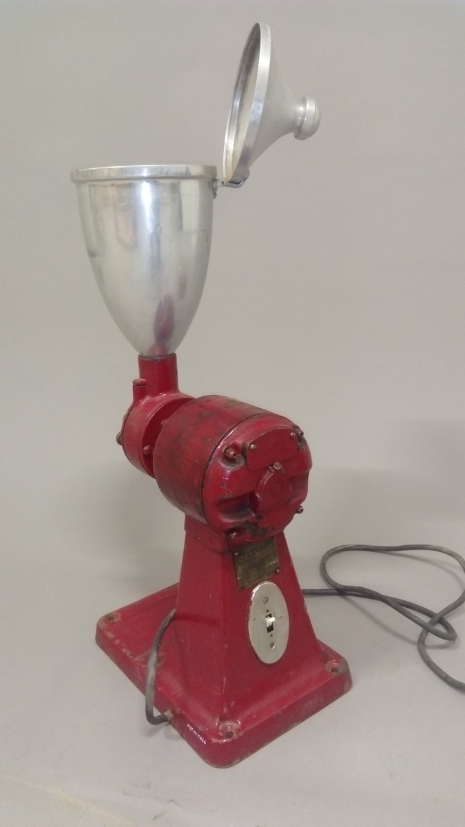 Elektrisk kaffekvern brukt i butikk. 
Kaffebønner helles i maskinen og males til kaffe, fortrinnsvis for kokkaffe.
Er komplett med avtagbar beholder for å fylle den ferdig malte kaffen i poser evt annet, samt ledning med støpsel. 

Maskina er rødlakkert, er slitt med noe rust og rester av olje eller fett.