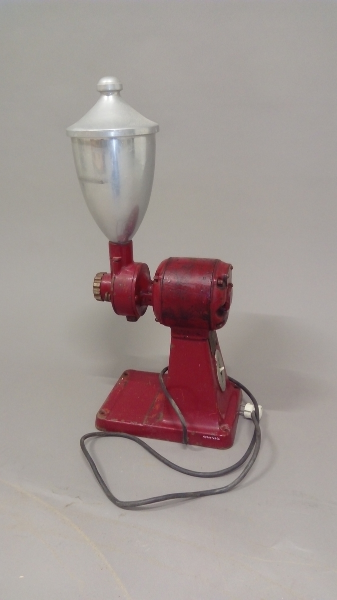 Elektrisk kaffekvern brukt i butikk. 
Kaffebønner helles i maskinen og males til kaffe, fortrinnsvis for kokkaffe.
Er komplett med avtagbar beholder for å fylle den ferdig malte kaffen i poser evt annet, samt ledning med støpsel. 

Maskina er rødlakkert, er slitt med noe rust og rester av olje eller fett.