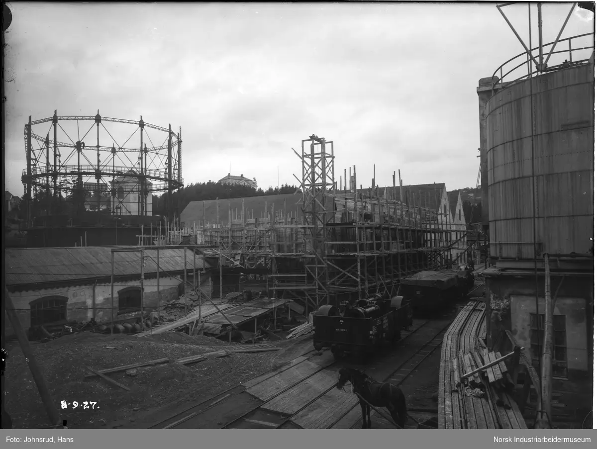 Kvelstoff og Renseanlegg under oppbyggingen. Hest står klar for last. Menn arbeider oppe i gasometer kontruksjon.