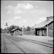 Vy över Dala Finnhyttan stationshus och godsmagasin med Garpenberg kyrka i bakgrunden.