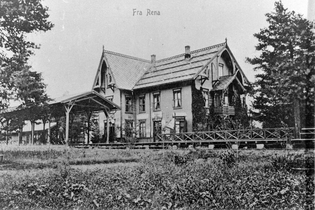 Rena jernbanestasjon, bygd i sveitserstil. Jernbanelinje og perrong i forgrunnen.