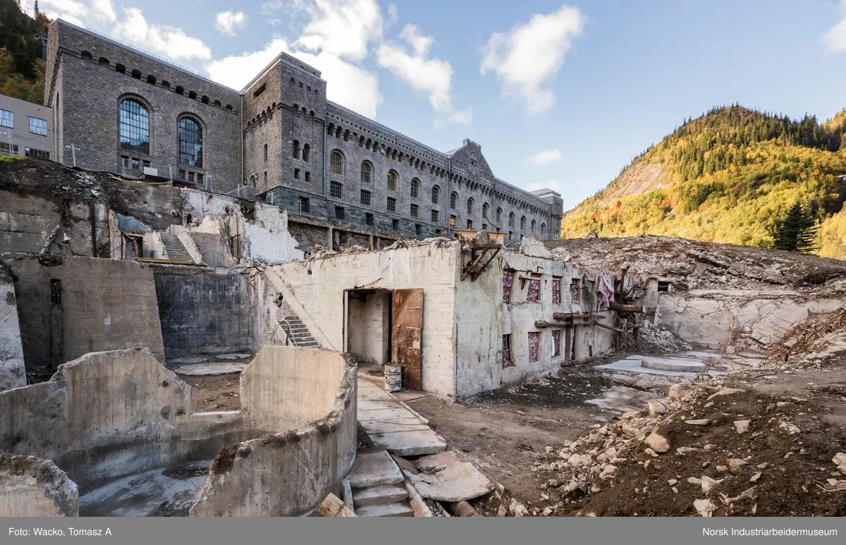 Bygningen var opprinnelig Vemork Hydrogenfabrikk som var plassert fem meter foran Vemork gamle kraftstasjon. Bygget var i betong i 8 etasjer. Driften i bygget stoppet i 1971 og ble i 1977 revet ved sprengning. Telemark Fylkeskommune initierte en utgravning på tomten for om mulig å finne rester etter den gamle kjelleren i 2017. 18.09.2017 startet arbeidet og kjelleren ble i november funnet inntakt.