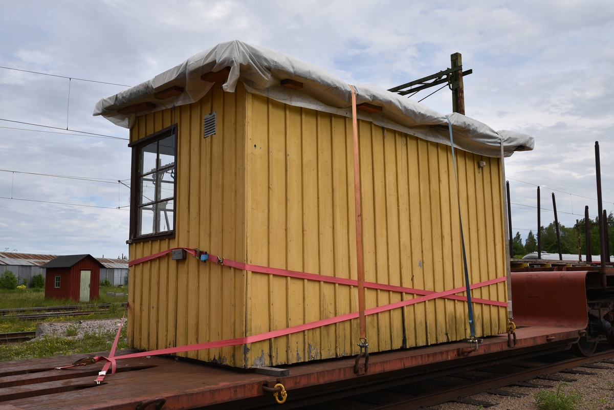 Hållplatskur från Tjunnaryd. Målad i ljusgul kulör med ljusgrå dörr, dörrfoder och fönsterfoder. Spröjsade fönster utmed hela framsidan, även på dörren, och delvis på sidorna.