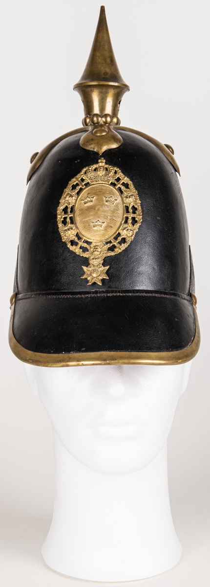 Kask m/1845 för infanteriet. Av pressat svartlackerat läder. hög välvd form med skärm och nackskycdd. Överst mässingspik med korsformat fäste. Skärmen mässingskantad. Framtill emblem i form av lilla riksvapnet i mässing. Hakremmar med fästen saknas. Spännbart "foder" av svart läder. Skrivet på nackskyddets insida. "Otto" samt "23 1/4".