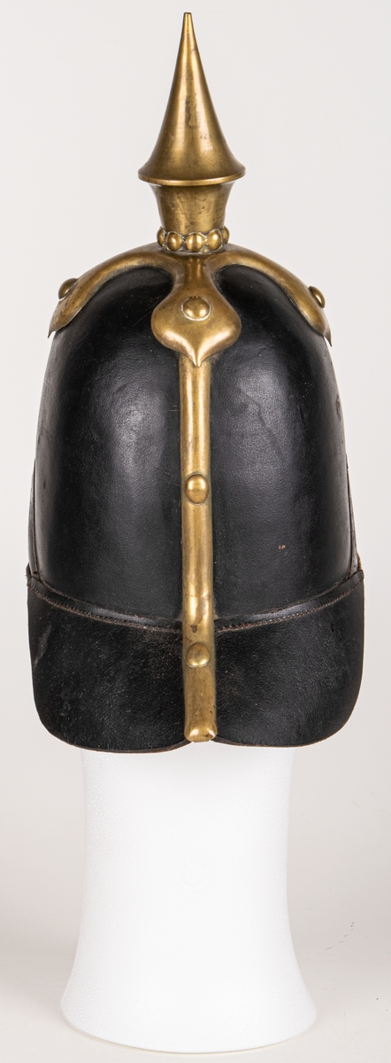Kask m/1845 för infanteriet. Av pressat svartlackerat läder. hög välvd form med skärm och nackskycdd. Överst mässingspik med korsformat fäste. Skärmen mässingskantad. Framtill emblem i form av lilla riksvapnet i mässing. Hakremmar med fästen saknas. Spännbart "foder" av svart läder. Skrivet på nackskyddets insida. "Otto" samt "23 1/4".