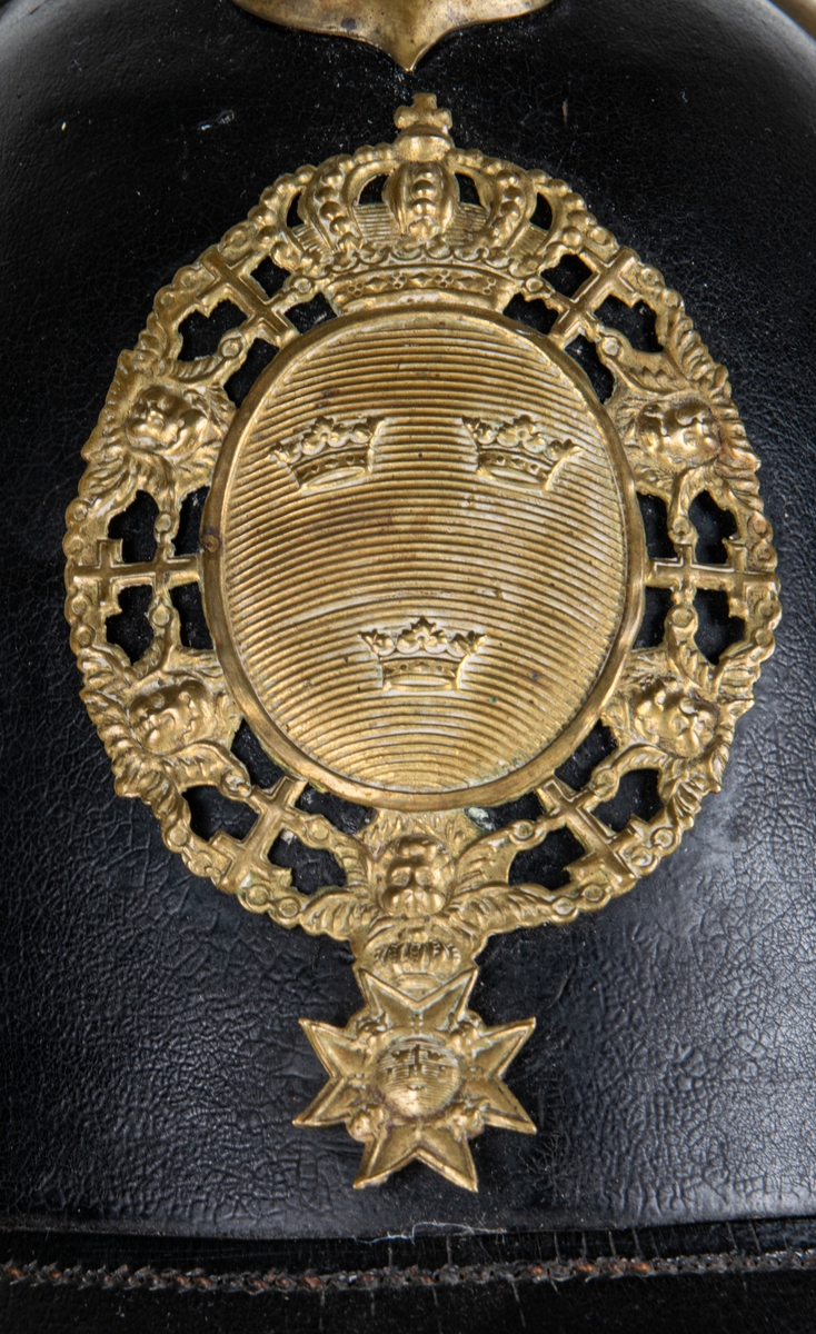 Kask m/1845 för infanteriet. Av pressat svartlackerat läder. hög välvd form med skärm och nackskycdd. Överst mässingspik med korsformat fäste. Skärmen mässingskantad. Framtill emblem i form av lilla riksvapnet i mässing. Hakremmar med fästen saknas. Spännbart "foder" av svart läder. Skrivet på nackskyddets insida. "Otto" samt "23 1/4".