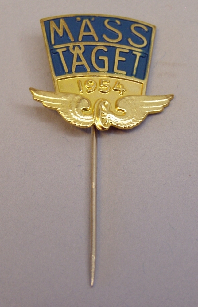 Kavajnål: "MÄSSTÅGET 1954" i guld mot blå botten, med Statens järnvägars emblem nedtill.