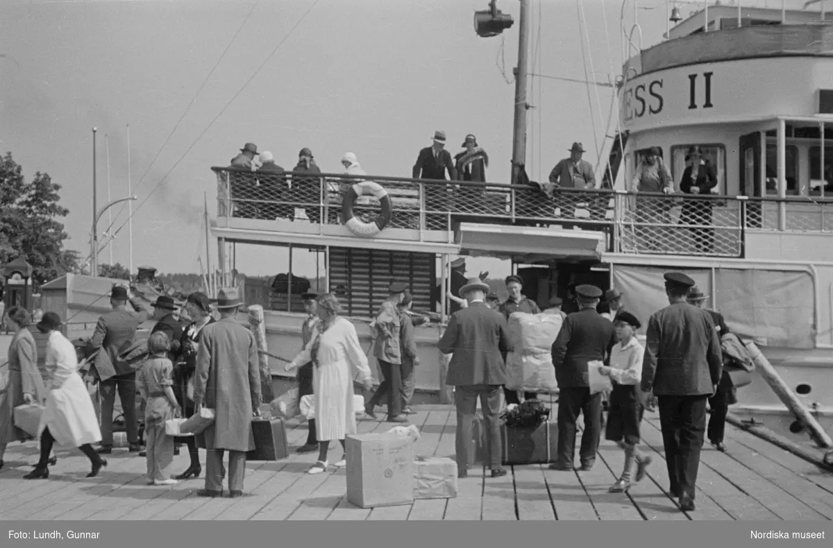 Motiv: Stockholm - Vaxholm;
Människor på en brygga med skylt "Edlunda", en segelbåt, människor på en brygga med skylt "Höganäs".

Motiv: Vaxholm;
Människor står på en brygga och en båt lägger till, en segelbåt, två män lyfter backar med flaskor på en brygga, folksamling vid möbler utställda på en grusplan (troligen en auktion).