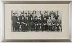 Trashalla-gänget år 1947. Gruppbild med personal från minapteringsverkstaden vid Trashalla, Marinkommando Syd. Fotografi 145x345 mm ramat i försilvrad träram med silverplåt (R 9) och texten: 