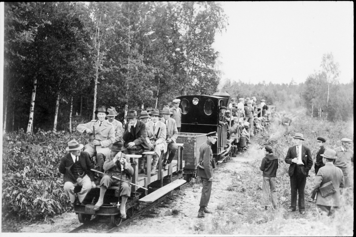 Kunglig älgjakt i Böda kronopark. Gustav V sitter på ett av "Kungavagnens" säte. Vid "tendern" står lokeldare Julius Svensson, i lokhytten ses lokförare Elis Ekholm. Mannen i uniform i mitten är jägmästare Per-Gunnar Arne. Initiativtagaren till skogsarbetarefackföreningen och landstingspolitiker Ragnar Persson står vid sidan av spåret.