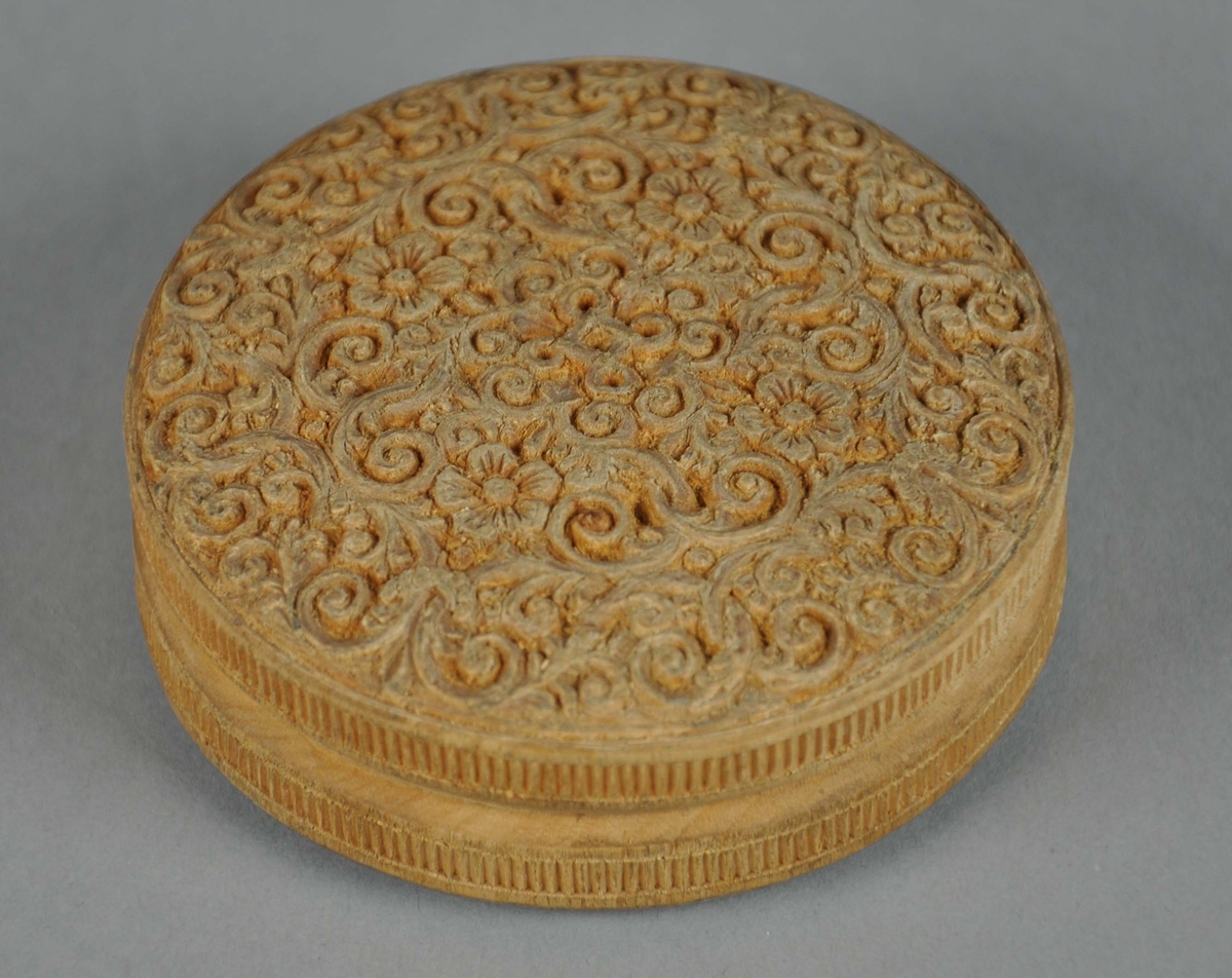 Rund eske av tre, med lokk. På lokket er det symmetriske treskjæringer av akantusmønster og blomster, med valknute på midten. Under esken er det konsentriske sirkler. På siden av esken og på siden av lokket er det border med tverrlinjer.
