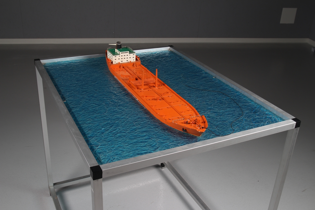 Modell av tankskip, såkalt bøyelaster - bygget i plast og montert på "sjø" av ruglet glassplate.