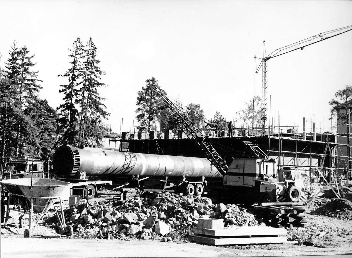 Montering av skorsten på regementets nya värmecentral den 10 oktober 1972.
Obs. Tio bilder.
Bild 1: Fundamentet på vilken den stora skorstenen skall skruvas fast.
Bild 2: Övre halvan av skorstenen under förflyttning till sin monteringsplats.
Bild 3: Nedre halvan av skorstenen håller på att lastas av från lastbilen. I bakgrunden syns den nya byggnaden till maskincentralen.
Bild 4: Nedre halvan läggs ned på stöd.
Bild 5: Den övre halvan av skorstenen, på yttersidan syns påsvetsade plåtspiraler för vindstabiliseringen.
Bild 6: Det krävdes kraftiga kranar för att klara alla lyft. I bakgrunden syns by 10 (Sörmlandssalen, markan och ubefmäss)
Bild 7: Flera kranar i samverkan för att få den nedre skorstenen i rätt läge.
Bild 8: Nu är skorstenen hopsatt och lyftet påbörjat.
Bild 9: Lyftet fortsätter, i förgrunden dom två oljecisternerna.
Bild 10: Nu står skorstenen på plats.