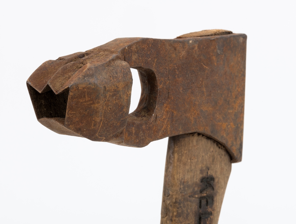 Øks - brukt til merking av fløtingstømmer i målings- og annammingsprosessen som foregikk langs vassdragene i overgangsfasen mellom vinter og vår, da tømmerstokkene etter måling formelt skiftet eier - fra skogeieren som hadde organisert hogst og framkjøring til sagbruk eller treforedlingsbedrift, som kjøpte tømmeret med sikte på videre bearbeiding til produkter som var salgbare på et større marked. 

Øksehodet (den smidde delen) er 14,2 centimeter høyt fra eggpartiet til nakken. Nakkedelen er 7,9 centimeter lang, 2,5 centimeter bred bakerst og 2,3 centimeter bred foran. Øksenakken er noenlunde plan i lengderetningen. På venstre side av den nedre delen av øksehodet (bladet) er det utsmidd en 3,5 centimeter høy «sko» med profilert, fasslipt egg. Denne eggen ble slått inn i yteveden på fløtingsvirket, der den etterlot seg en profilert forsenkning, et symbol som tjente som sorteringsgrunnlag ved lenseanleggene i den nedre delen av vassdraget. På denne øksa minner eggprofilen om omrisset av ei krone. På høyre side av øksehodet finner vi smedstempelet «K. KNUDSEN  MJØNDALEN» samt avbildninger av medaljer denne produsenten hadde oppnådd på utstillinger. Øksehodet er rustent og stempelet er vanskelig lesbart.

Denne øksa har et cirka 60 centimeter langt, noenlunde rett treskaft. Som økseskaft flest er det bredest i høyderetningen og smalest i bredderetningen i den fremre enden, der den er skjeftet. Den bakre delen av skaftet er mer rundoval. Den fremre skaftenden er kilet med en trekile som skulle redusere faren for at øksa løsnet fra skaftet under merkingsarbeidet. Det forkortete firmanavnet «KELL-PARTINGTON» er påført den venstre sida av skaftet (sett i øksebrukerens perspektiv) ved hjelp av svijernstempel. Dette indikerer at øksa har vært brukt til å merke tømmer som ble innkjøpt på vegne av The Kellner Partington Paper Pulp Co. Lim., et engelsk selskap som fram til 1918 eide Borregaard-fabrikken i Sarpsborg. Navnet fortsatte å figurere på merkekartene også etter at Borregaard fikk norsk eierskap, jfr. «Merkekart 1953 for Glommen» i Julius Nygaards skogalmanakk 1954. 

Litt generell informasjon om bruken av merkeøkser i skogbruket finnes under fanen «Opplysninger».