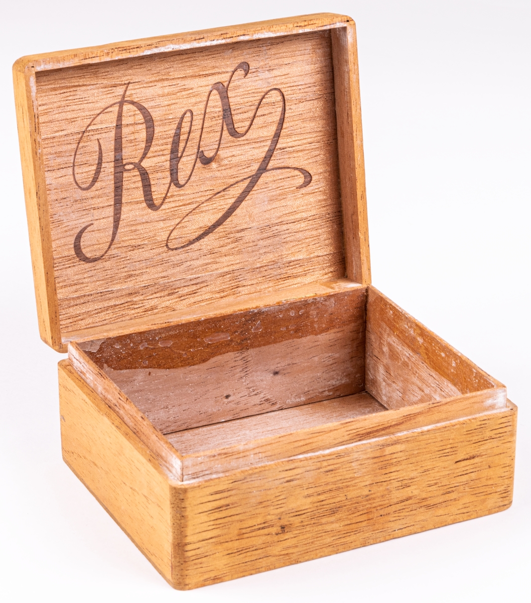 Ask av trä märkt med lock försett med två gångjärn av mässing. Rex som text på locket. Har använts som nipperask.