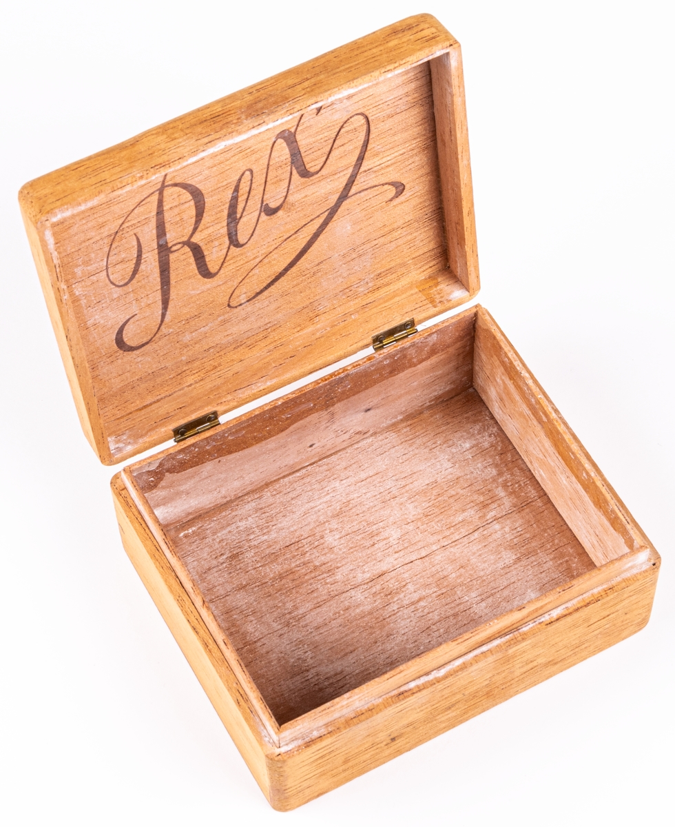 Ask av trä märkt med lock försett med två gångjärn av mässing. Rex som text på locket. Har använts som nipperask.