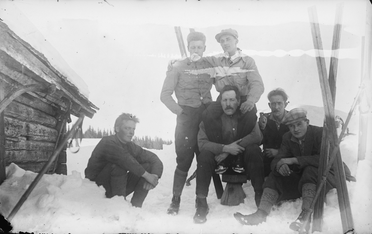 Noe karer på ski i Gausdal Vestfjell, fotografert utenfor ei gammel hytte. Fotograf Karl Olav Moe sitter som nr 2 fra høyre.