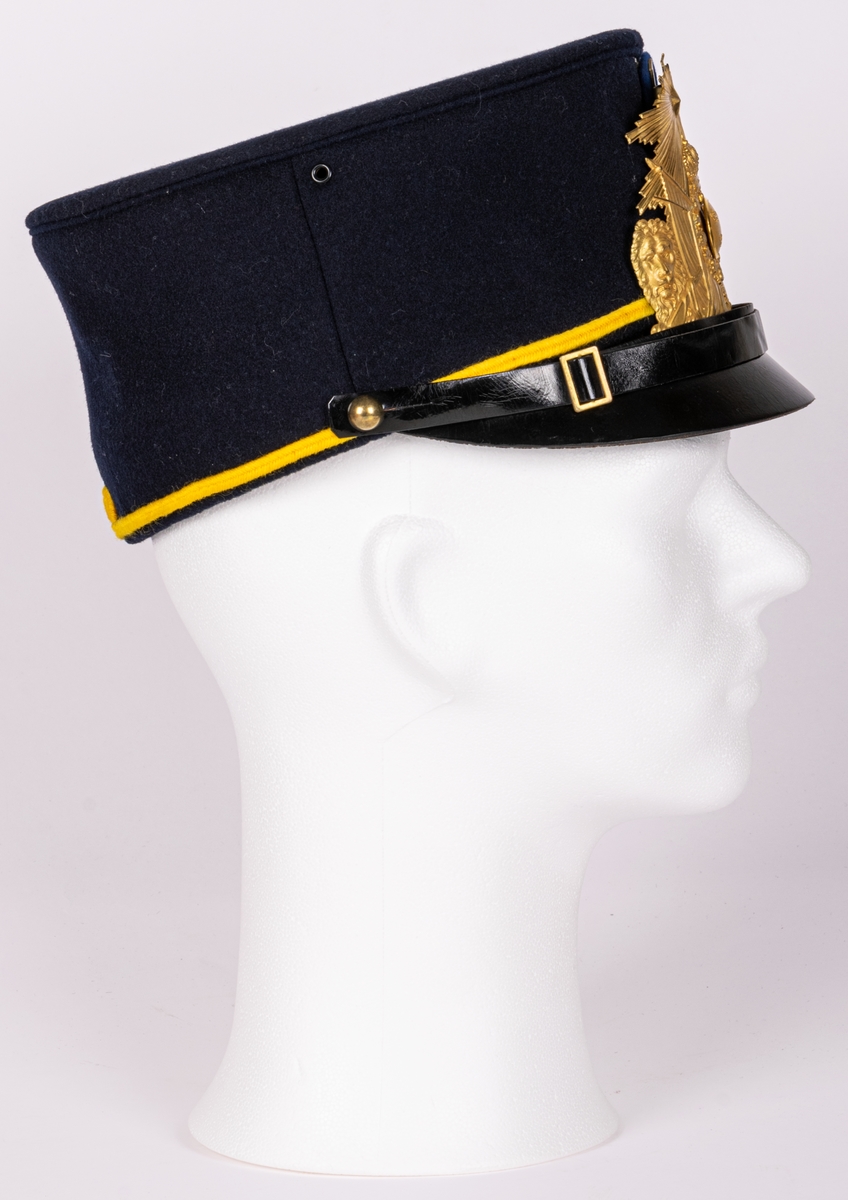 Mössa, uniformsmössa, blå med stor mässingsbricka, lilla riksvapnet omgivet av lejon, flaggor och med kungl. krona ovanför samt 5-uddig stjärna med strålar. Överst plymfäste med tagelplym. M/1899.