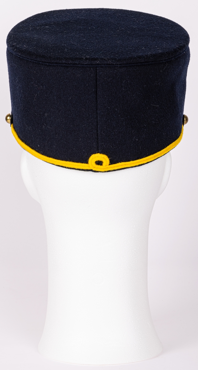 Mössa, uniformsmössa, blå med stor mässingsbricka, lilla riksvapnet omgivet av lejon, flaggor och med kungl. krona ovanför samt 5-uddig stjärna med strålar. Överst plymfäste med tagelplym. M/1899.