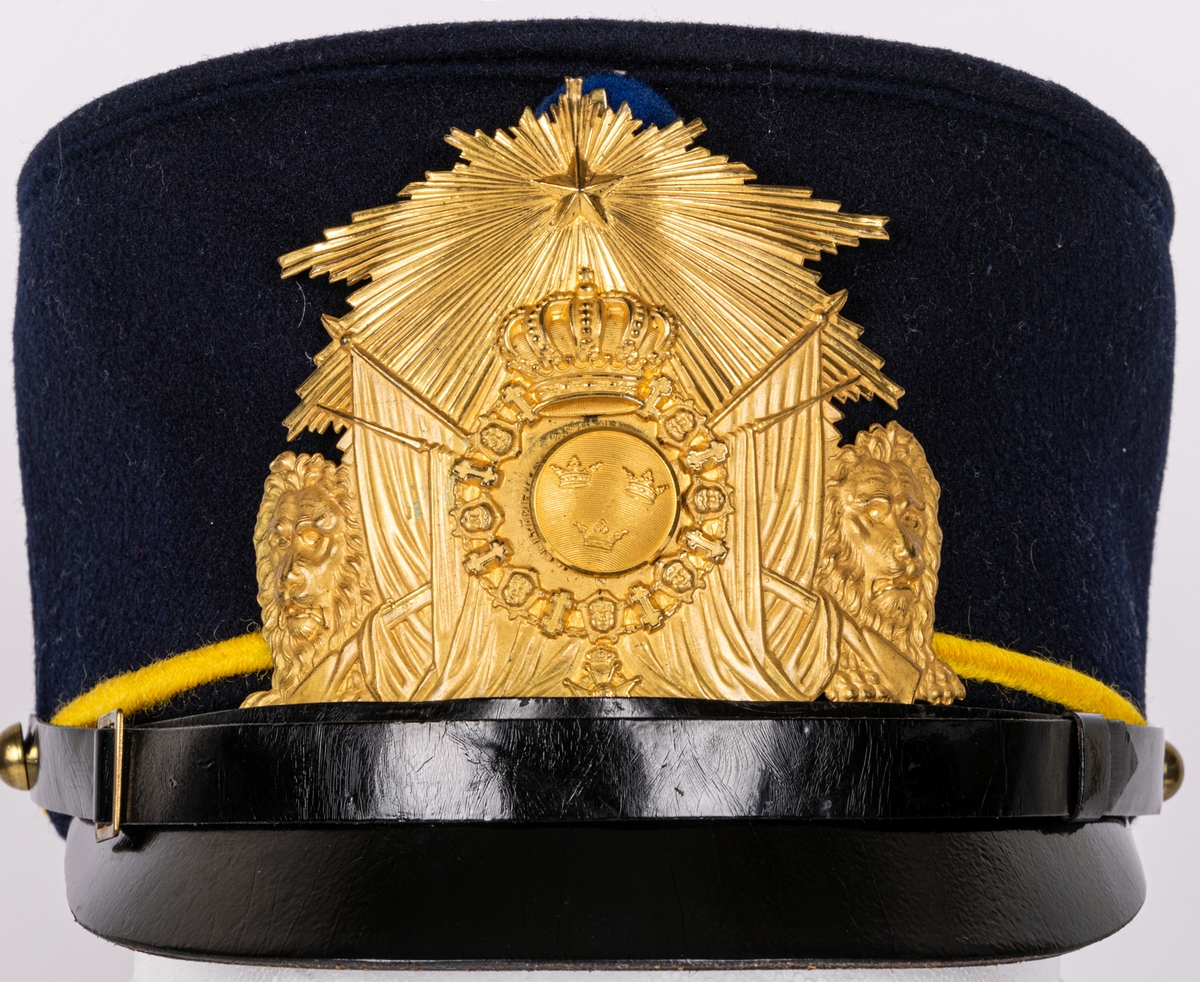 Mössa, uniformsmössa, blå med stor mässingsbricka, lilla riksvapnet omgivet av lejon, flaggor och med kungl. krona ovanför samt 5-uddig stjärna med strålar. Överst plymfäste med tagelplym. M/1899.