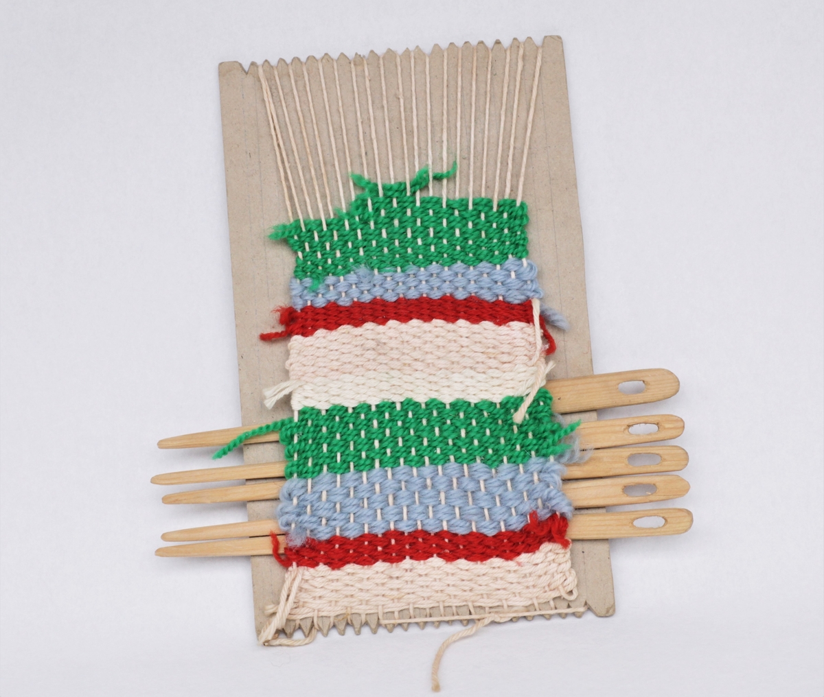 Hjemmelaget vev med pinner. Kartongplate, hyssing som renning og ulltråd som vev.