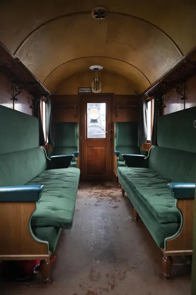 Interiør fra en andre-klasses passasjervogn på Urskog-Hølandsbanen. To tre-seters sofaer i flaskegrønn plysj er plassert mot hverandre i vognens lengderetning. To stoler har ryggen mot kortveggen, en på hver side av utgangsdøren.
