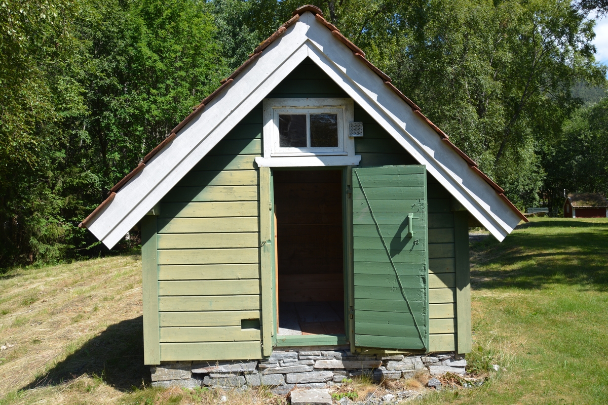 Bygning i eit rom, reisverk. Liggande panel. Dør i gavlveggen. Vindauge over døra. Panel måla mintgrøn (som bygningane i Singerheimen, Olden)