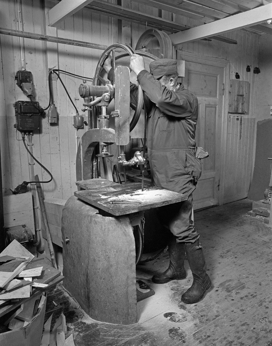 Bygging av fløterbåt i Glomma fellesfløtingsforenings verksted Breidablikk ved kommunesenteret Flisa i Åsnes i november 1984. Båttypen ble for øvrig kalt «Flisabåt», men denne modellen var egentlig utviklet av John Dybendal (1904-1985) omkring 1930. Målet var å kunne levere en robåt som passet i elva Flisa. Dybendal bygde sjøl slike båter fram til 1949. Glomma fellesfløtingsforening hadde vært en viktig kunde hos Dybendal, og da han gav seg som båtbygger ble virksomheten flyttet til denne virksomhetens verksted for Solør-regionen, hvor båtbygging ble vinteraktivitet for et par av karene som hadde vassdraget som arbeidsplass sommerstid. Det var maler til alle båtdeler, og skroget ble bygd på tverrmaler som ble festet til kjølen. Dette var hjelpemidler som gjorde det mulig for fløtere med reletivt liten handverkserfaring å bygge denne båttrypen og oppnå den standardiserte formen som fløterkameratene var vant med. De fleste flisabåtene fikk jernspanter, for det var krevende å finne de krokvokste emnene som gav de beste spantene. Ettersom Norsk Skogbruksmuseum dokumenterte båtbygginga ville karene likevel bruke trespanter på denne siste båten de bygde. Da dette fotografiet ble tatt monterte Lars Bernhard Olastuen (1927-1998) blad på bandsaga.

Båten som var under bygging da dette fotografiet ble tatt ble seinere overlatt til Norsk Skogbruksmuseum, der den fikk nummer SJF.07823 i gjenstandssamlinga. Den er 518 centimeter lang og 153 centimeter bred. Odd Jensen har seinere lagd oppmålingstegninger, som også finnes i museets arkiv.