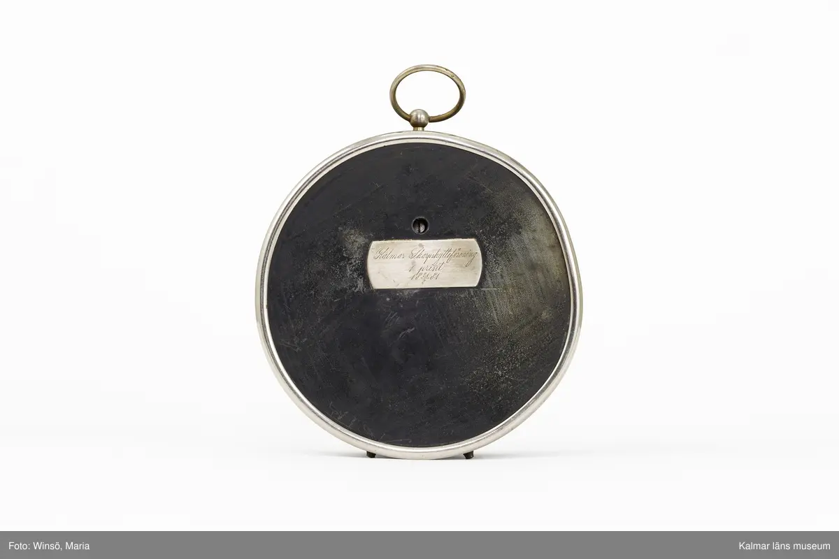 KLM 46367. Barometer, aneroidbarometer. För mätning av lufttryck. Fodral av metall och glas, delvis svartlackerat, mätverk av mässing. Rund form, tavla med skala från 69 till 80 samt från STORM till MYCKET TORT. Nedtill på tavlan: C. Hentzell Kalmar samt ett monogram. På baksidan en metallskylt: Kalmar Skarpskytteförening 1 priset 21/8 1881. Barometern har nedtill två små fötter samt upptill en ring för upphängning.