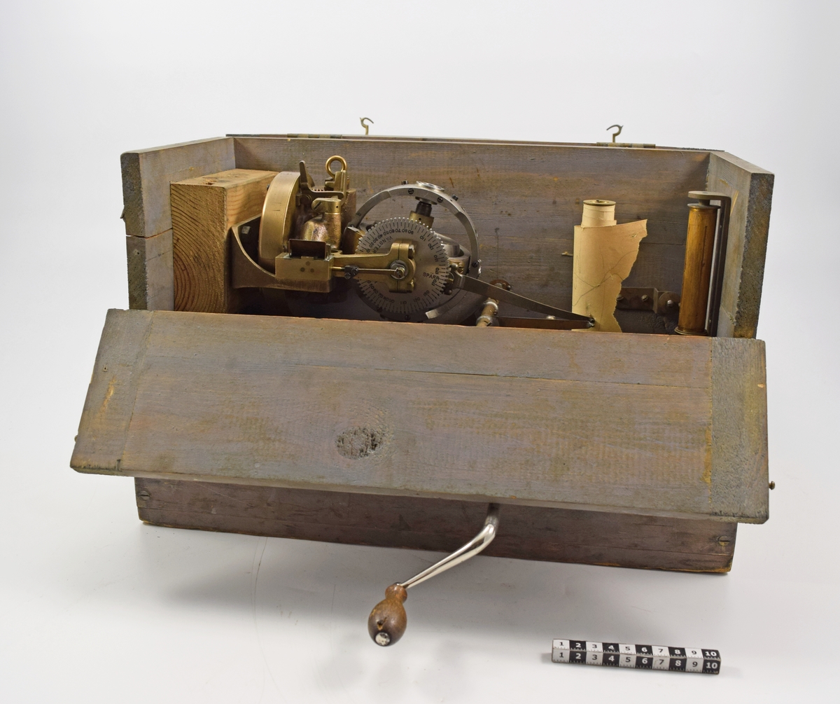 Gyroskop förvarat i gråmålad trälåda med lock samt ena långsidan öppningsbar med gångjärn och hakar. Till gyroskopet hör en skrivare som går att reglera med spak från lådans utsida. Vev med trähandtag tillkommer samt kopparrör med nippel (för att ge gyroskopet luft). Pappersetiketter på lådans utsida= "Fr Stockholms Centr 977" samt "Karlskrona".