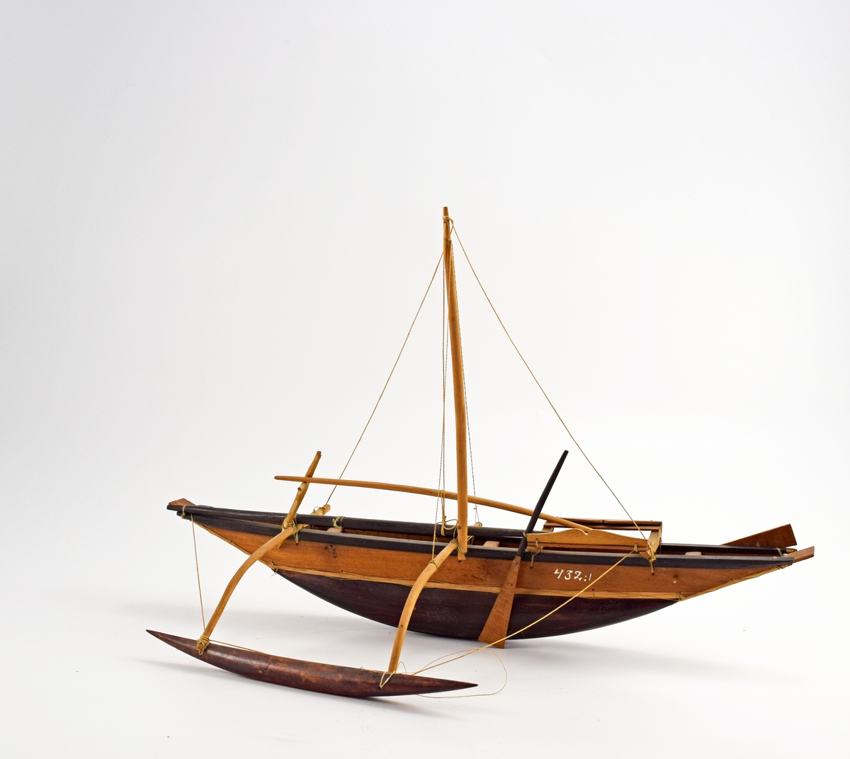Segelbåt med uteliggare Katamarangaa (Katamarang), modell. Försedd med 1 st mast och 2 st åror. Är målad med en svart rand vid relingen och svart undervattenskropp. Modellen är inköpt under Vanadis världsomsegling 1883-85 (på Ceylon) och sedan skänkt till samlingarna av löjtnant Leopold Karlsson (Marinen) år 1927.