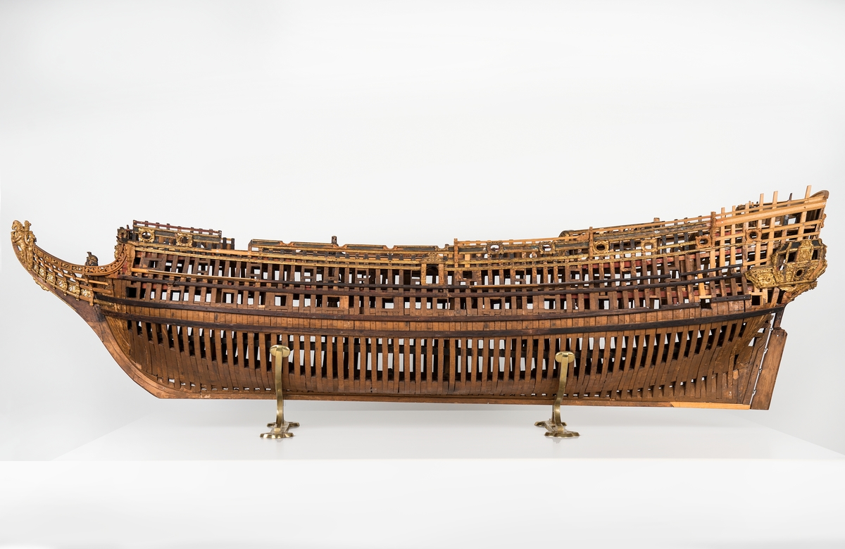 This unplanked model of a three-decker can be dated to c. 1660 and is one of the world's oldest models of a warship. Although not definitively identified, recent research links it to the Swedish ship *Riksäpplet*, designed by the English master shipwright Francis Sheldon and launched in 1661.     
The model was possibly made for Sheldon, who came to Sweden in 1659. He was one of a number of English shipwrights employed by the Swedish crown during the period. Previously, most Swedish warships had been built in the Dutch style.

From around 1660, the English Royal Navy’s administrators commissioned models that were accurately detailed and true to scale. These miniatures, which came to be called Navy or Admiralty Board models, had an unplanked lower hull to emphasise the shape of the underwater body. 

The model was restored by rear-admiral Jacob Hägg in the late 1890s. Missing parts have been reconstructed using lighter coloured wood.

3D model produced by Adam de Kaminski and Vasilis Haroupas for SMTM, 2023
