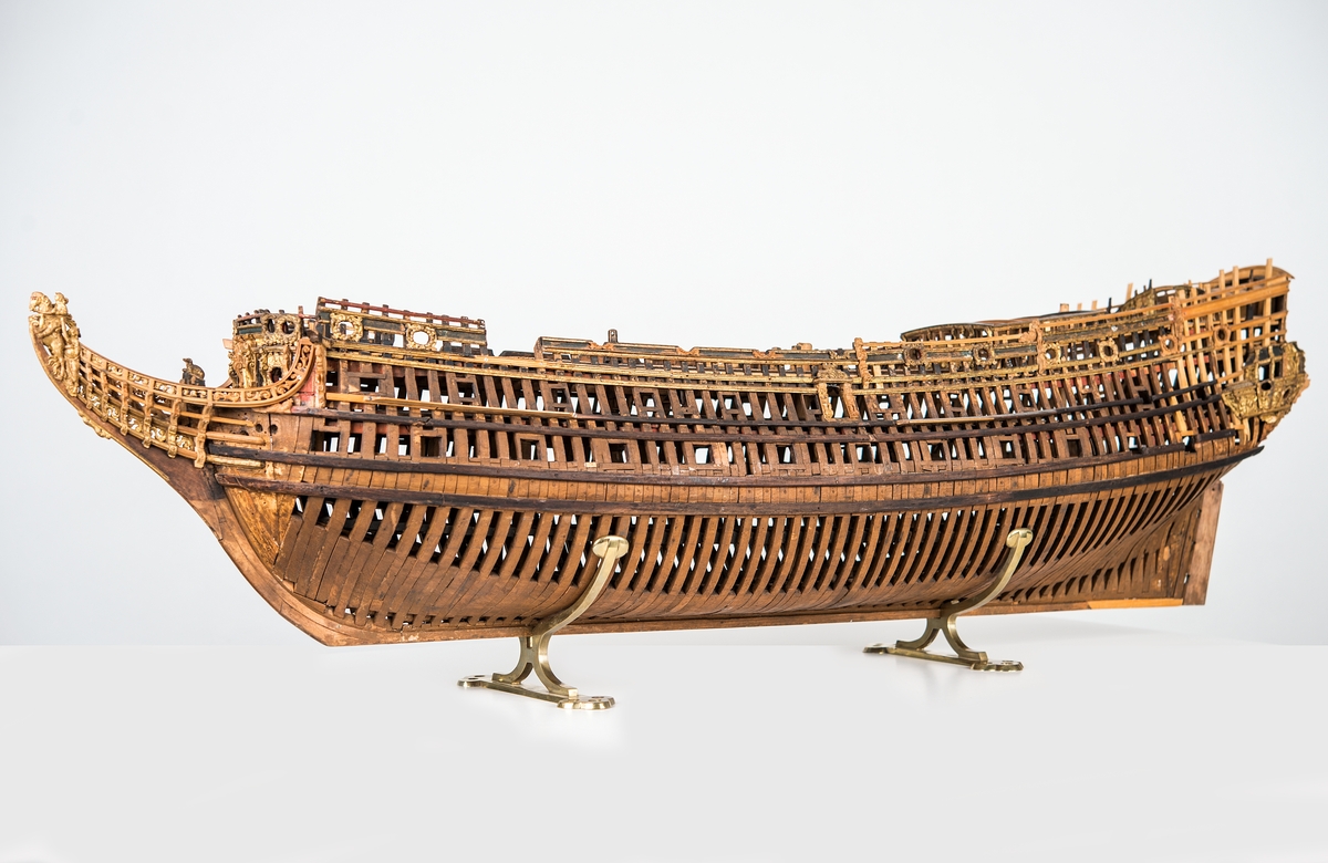 This unplanked model of a three-decker can be dated to c. 1660 and is one of the world's oldest models of a warship. Although not definitively identified, recent research links it to the Swedish ship *Riksäpplet*, designed by the English master shipwright Francis Sheldon and launched in 1661.     
The model was possibly made for Sheldon, who came to Sweden in 1659. He was one of a number of English shipwrights employed by the Swedish crown during the period. Previously, most Swedish warships had been built in the Dutch style.

From around 1660, the English Royal Navy’s administrators commissioned models that were accurately detailed and true to scale. These miniatures, which came to be called Navy or Admiralty Board models, had an unplanked lower hull to emphasise the shape of the underwater body. 

The model was restored by rear-admiral Jacob Hägg in the late 1890s. Missing parts have been reconstructed using lighter coloured wood.

3D model produced by Adam de Kaminski and Vasilis Haroupas for SMTM, 2023

