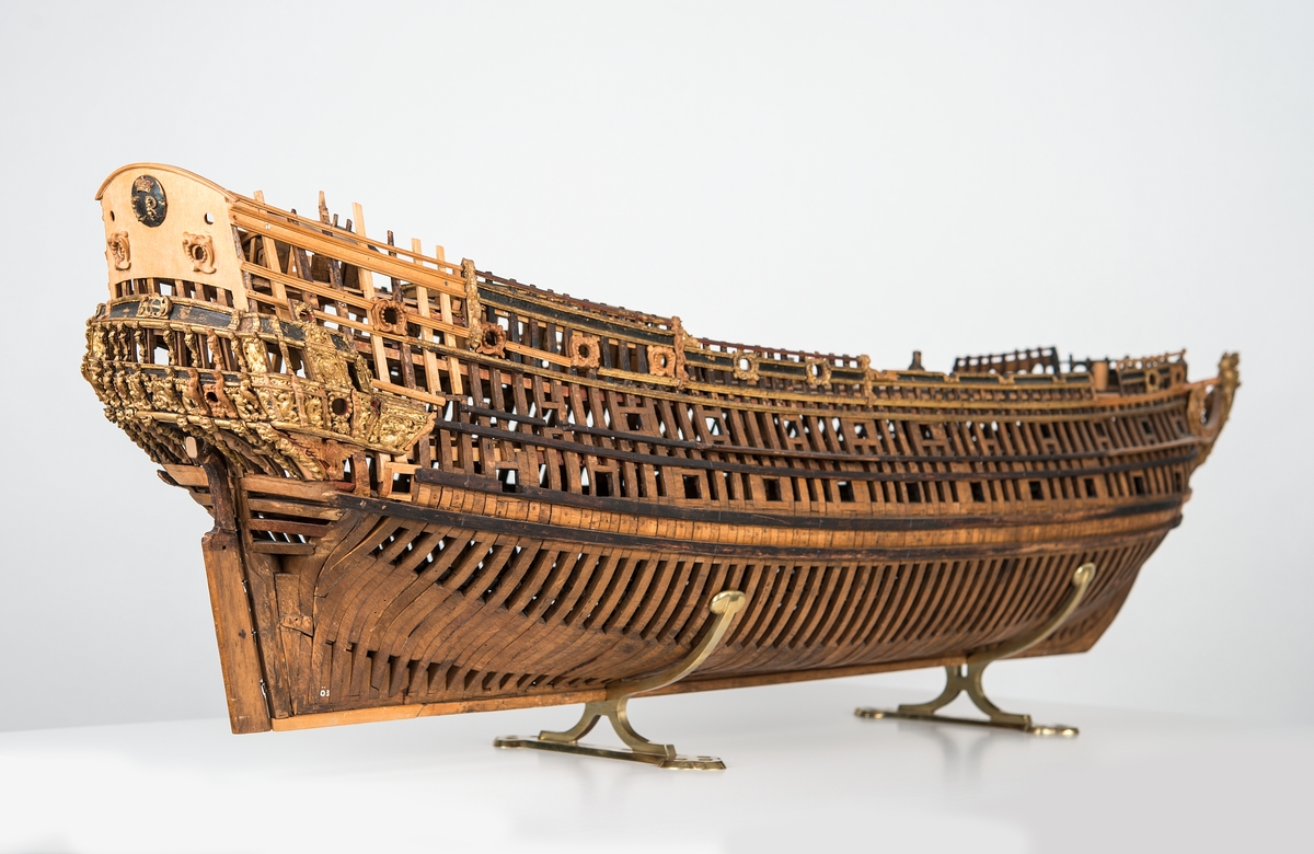 This unplanked model of a three-decker can be dated to c. 1660 and is one of the world's oldest models of a warship. Although not definitively identified, recent research links it to the Swedish ship *Riksäpplet*, designed by the English master shipwright Francis Sheldon and launched in 1661.     
The model was possibly made for Sheldon, who came to Sweden in 1659. He was one of a number of English shipwrights employed by the Swedish crown during the period. Previously, most Swedish warships had been built in the Dutch style.

From around 1660, the English Royal Navy’s administrators commissioned models that were accurately detailed and true to scale. These miniatures, which came to be called Navy or Admiralty Board models, had an unplanked lower hull to emphasise the shape of the underwater body. 

The model was restored by rear-admiral Jacob Hägg in the late 1890s. Missing parts have been reconstructed using lighter coloured wood.

3D model produced by Adam de Kaminski and Vasilis Haroupas for SMTM, 2023
