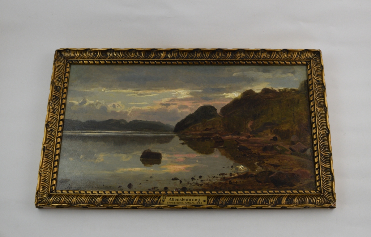 Landskapsmaleri med en fjord nede til høyre, en åsrygg til høyre og feler fjellrygger i bakgrunnen til venstre. Himmel med skyer og trolig en soloppgang. Skogsfjord i Mandal.