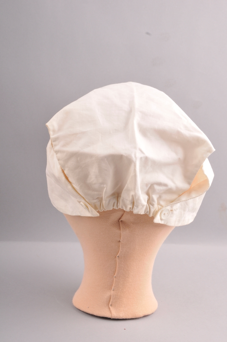 Lerretshette sydd med maskin og for hand. Strikk og rynka midt bak. Eit knapphol på kvar side med knapp slik at hetta blir knept saman bak. Hetta er laga i eit stykke. Dobbelt tøy. Avrunda framme. Lapp med talet to i nakken.