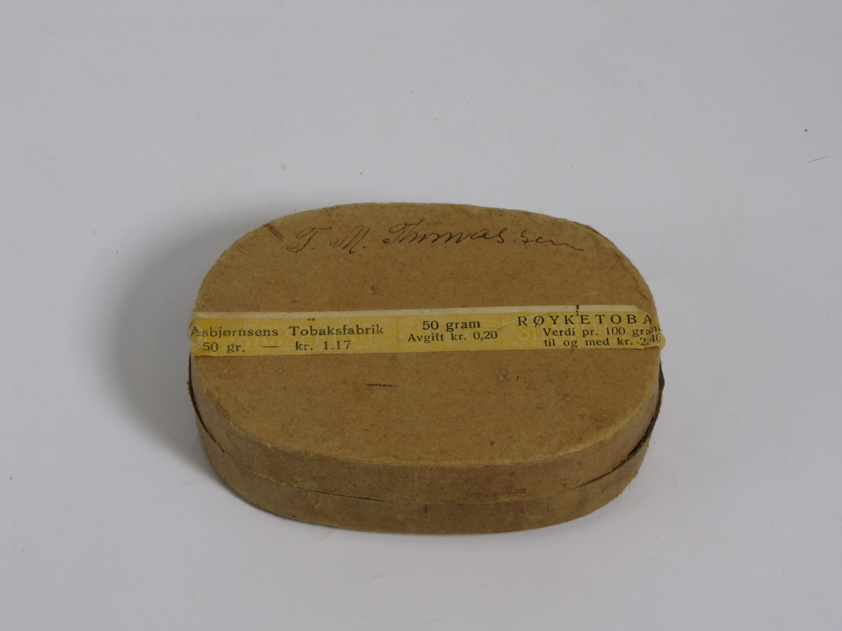 Tom tobakkseske i papp. Type "Karvet blad" fra A. Asbjørnsen, Christianssand S. Da den ble gitt til museet hadde den blitt brukt til oppbevaring av diverse småting (sikringer, sikkerhetsnål o.l.)