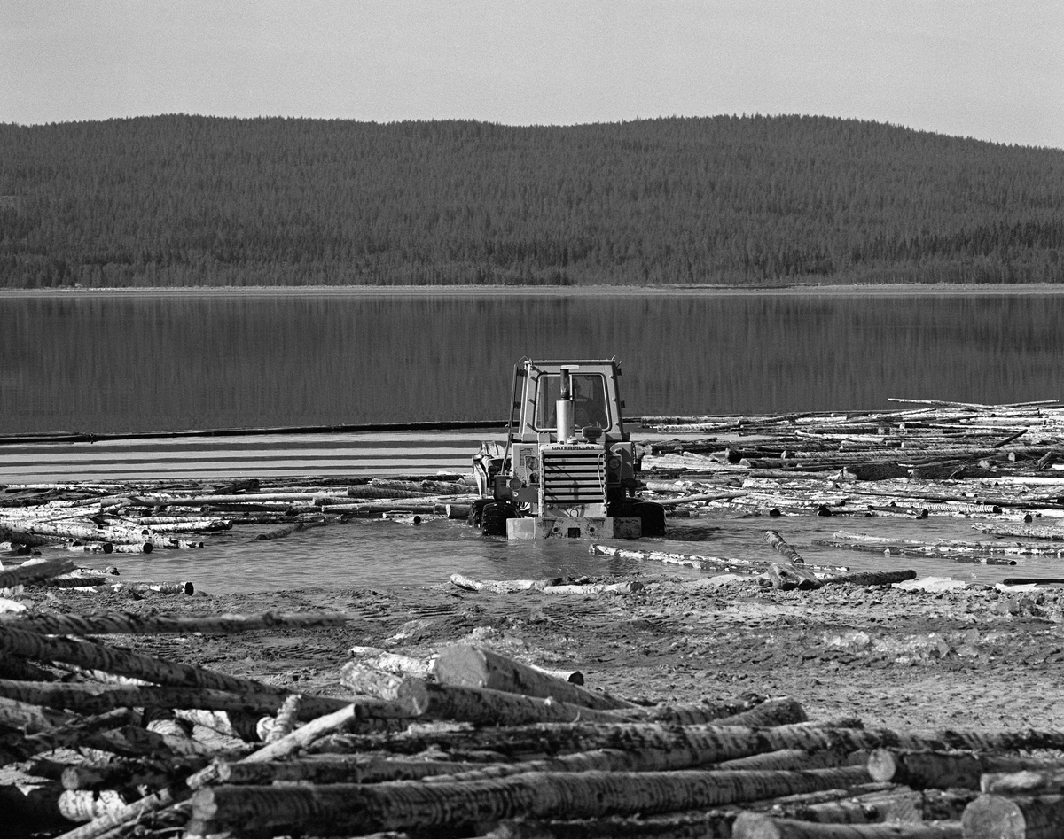 Hjullaster løfter ut i vannet ved Osmundsand ved Osensjøen i Nordre Osen, Åmot kommune, Hedmark våren 1984. Dette ble den siste sesongen det ble fløtet tømmer på denne innsjøen. Fløtinga i tilløpselva Nordre Osa, som har sitt utløp ved Osmund hadde opphørt 14-15 år tidligere, men mye tømmer fra dette området ble kjørt til Nordre Osen med lastebiler og lesset av på land på dette stedet. Etter at tømmerveltene var skjøvet ut i vannet, ble løstømmeret samlet i bommer, som ble buksert mot Valmen og elva Søndre Osas utløp fra sjøen, som ligger på vestsida. I 1984  var det 13 212 kubikkmeter som ble fløtet fra Osensjøen via Søndre Osa og Rena mot Glomma.